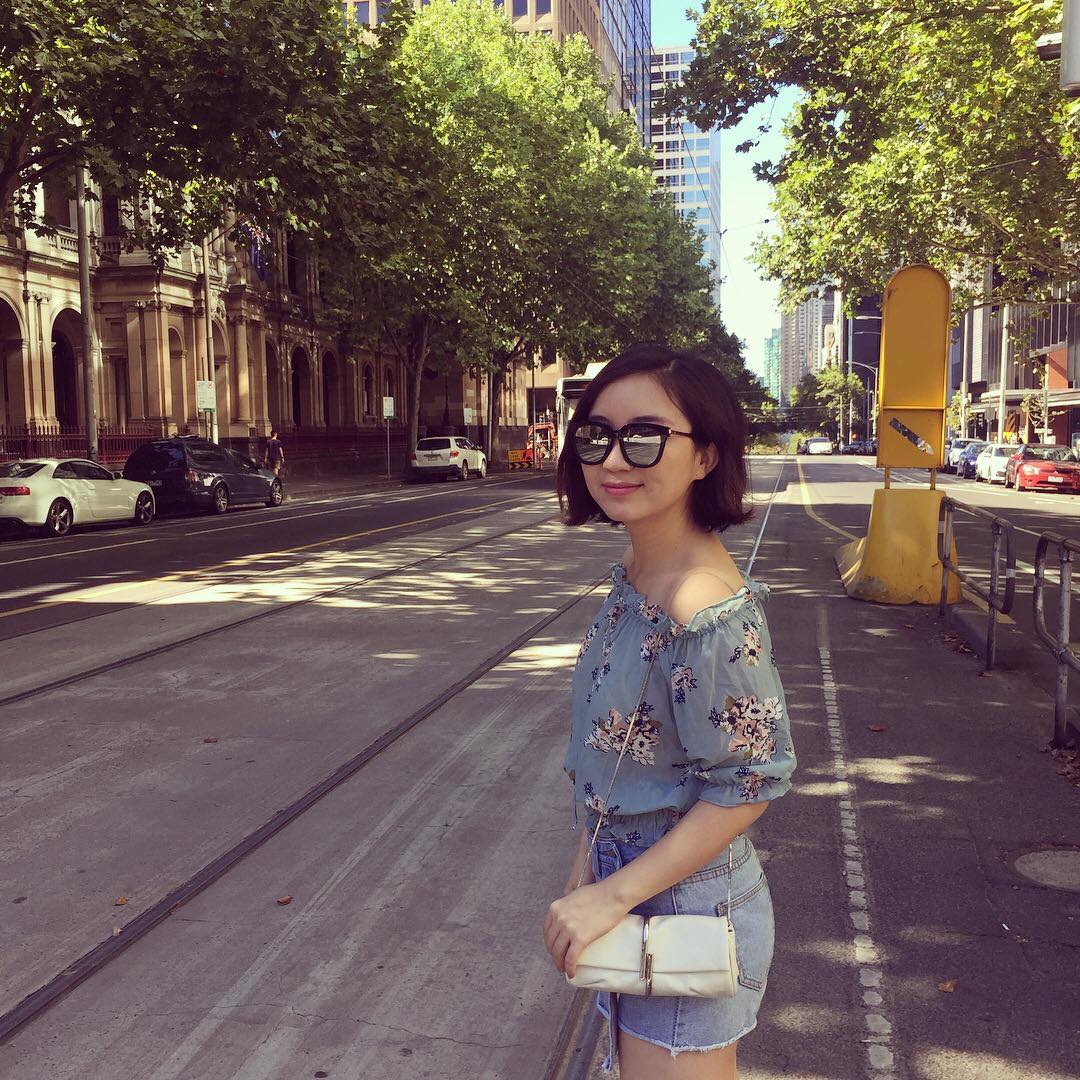 A young Chinese lady, wearing sunglasses, about to cross the road.