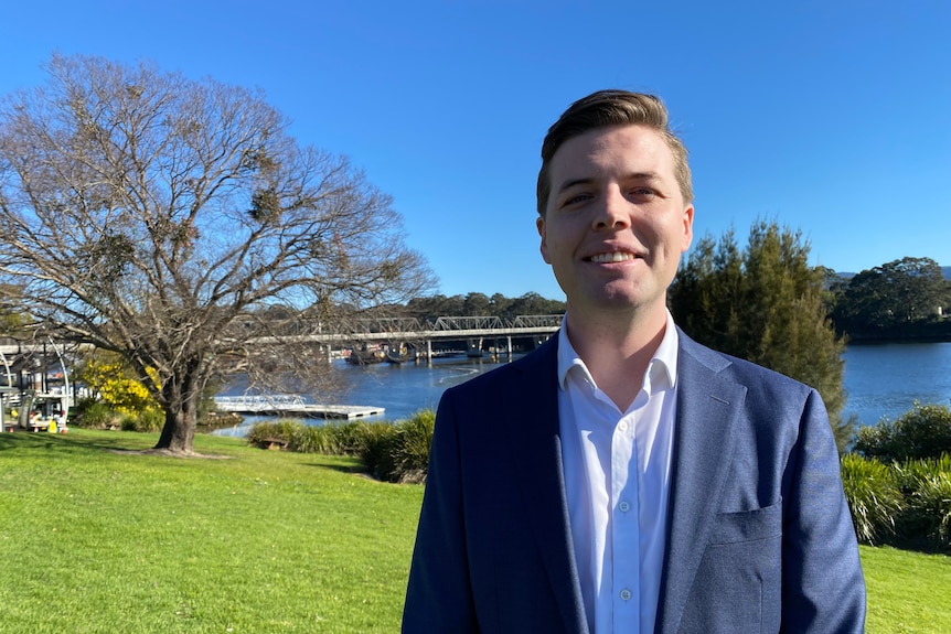 A smiling man wearing a suit on the foreshore of a river.