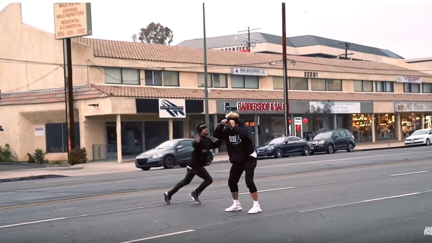 YouTuber Jake Paul stands in the middle of the road wearing a blindfold and facing oncoming traffic.