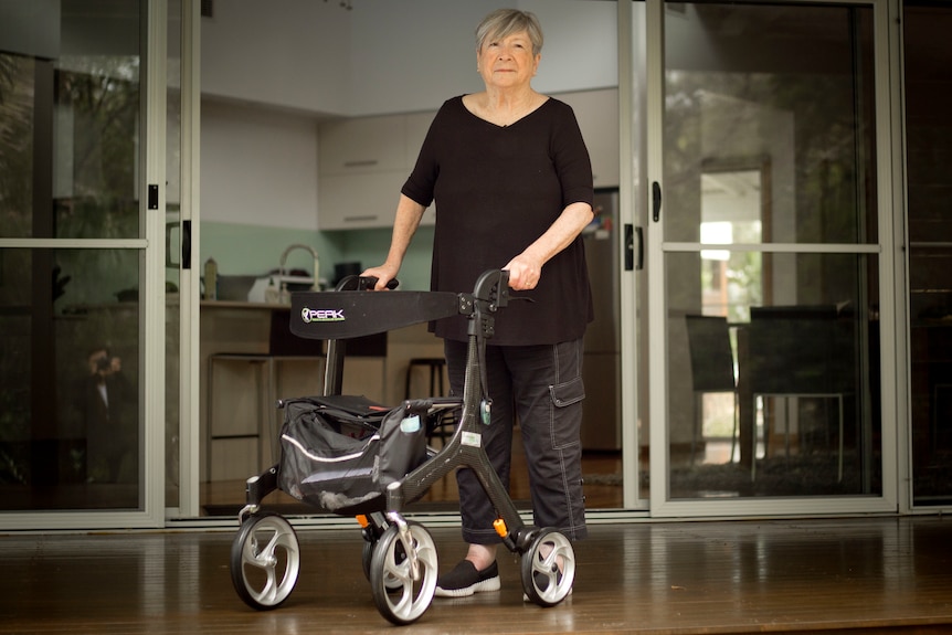 An older woman dressed in black standing up holding a walker