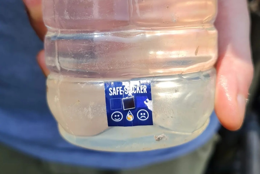A close-up photo of a hand holding a blue SAFE water sticker on a bottle.