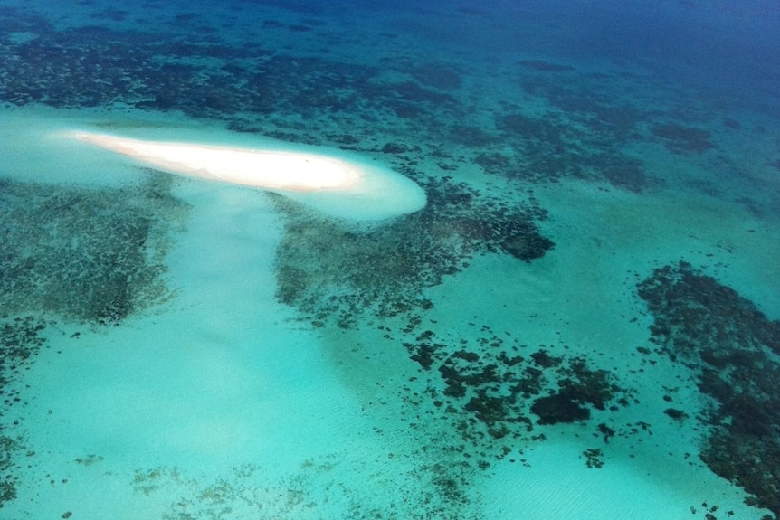 An aerial view of a white sand quay surrounded by blue waters and coral reef.