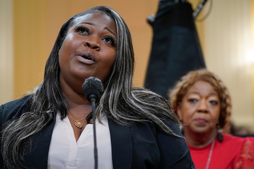 Shaye Moss speaking at a microphone with her mother in the background