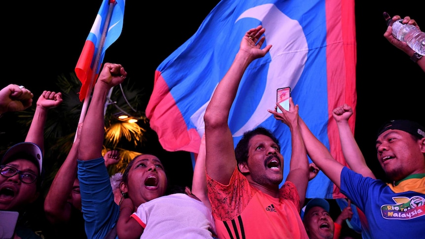 People celebrate against the backdrop of the Malaysian flag.