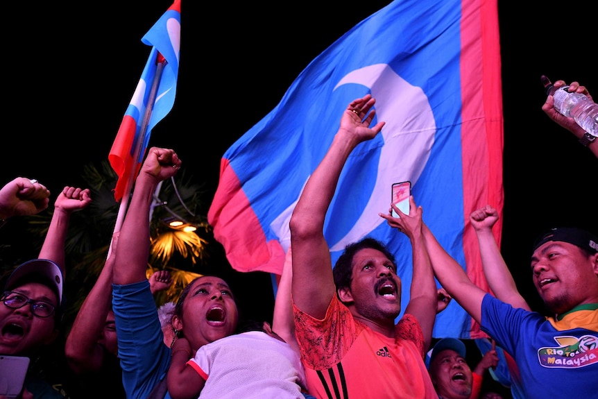 People celebrate against the backdrop of the Malaysian flag.