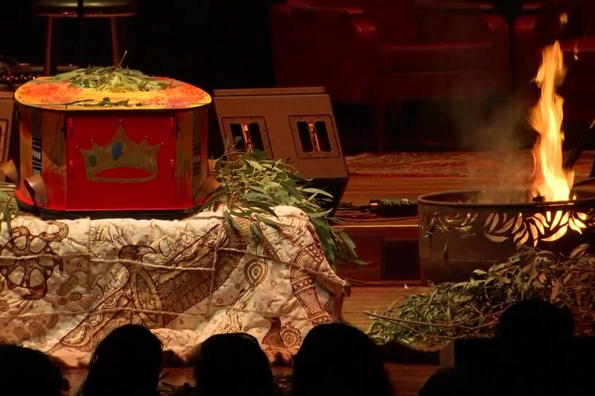 A coffin and fire sit on stage.