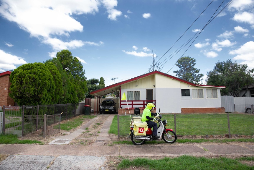 Australia Post employee on motorbike delivering mail in suburban street.