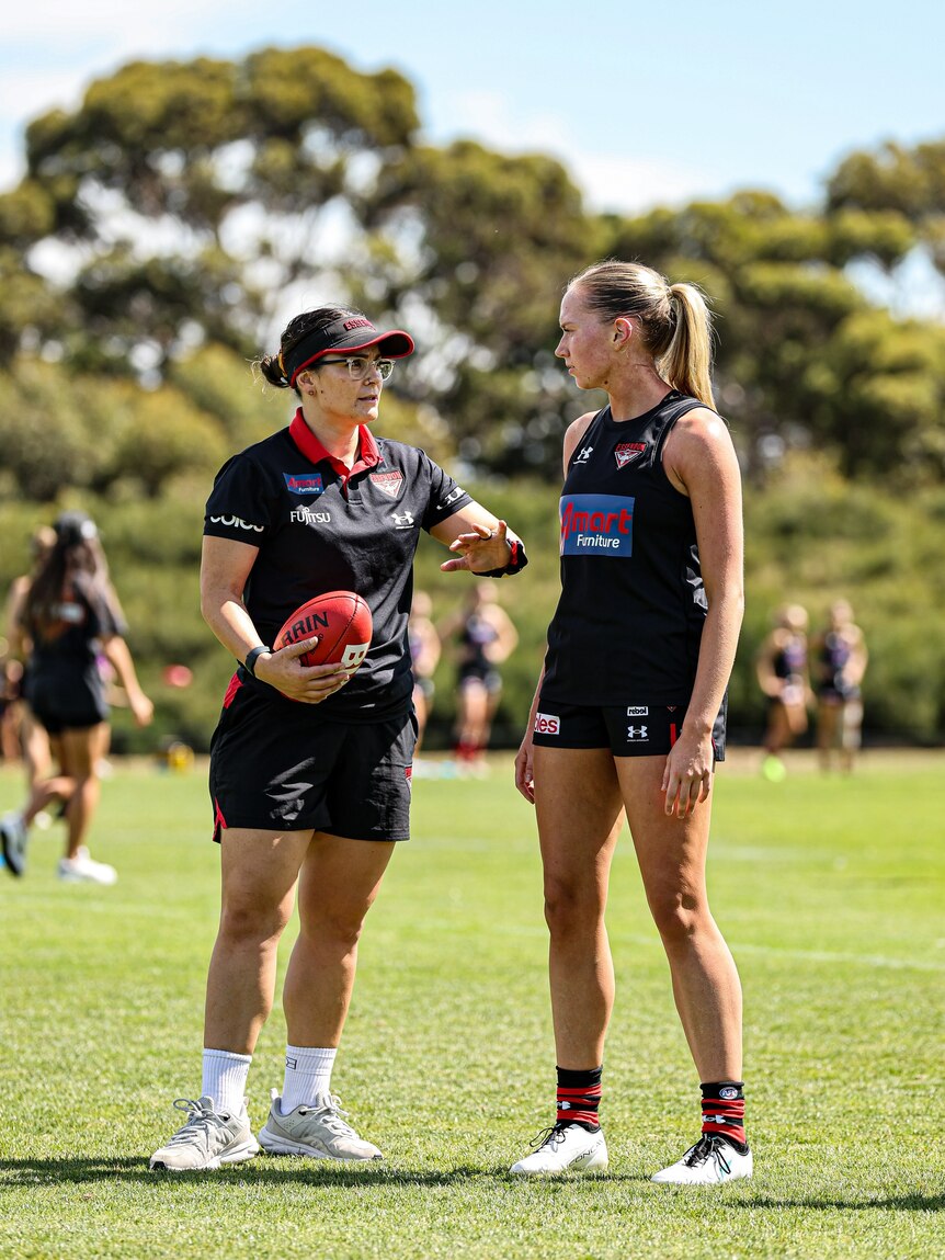 Jacara holds a footy as she trains a player on the field at Essendon FC. 