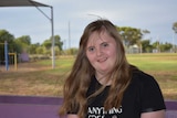 A close up of a girl with long blonde hair and blue eyes smiles while sitting on a purple bench