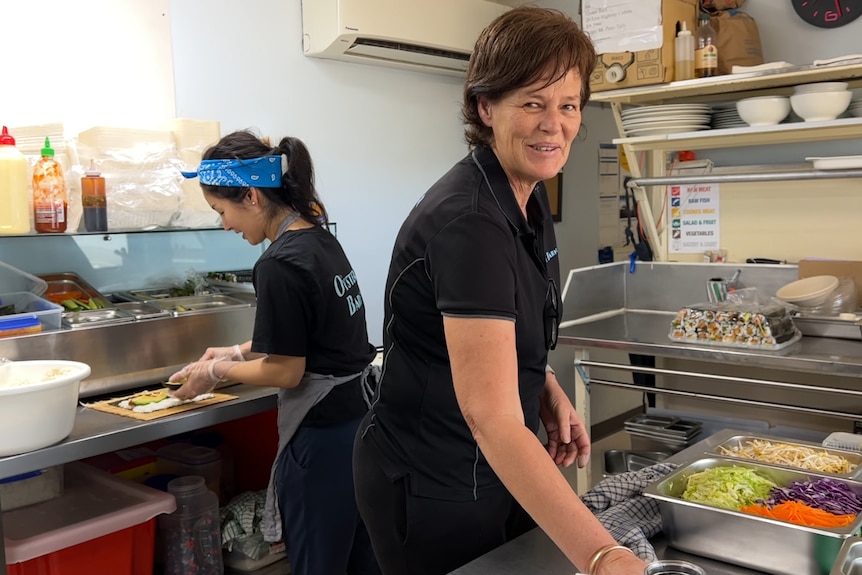 Two women working in a kitchen. One smiles at the camera.