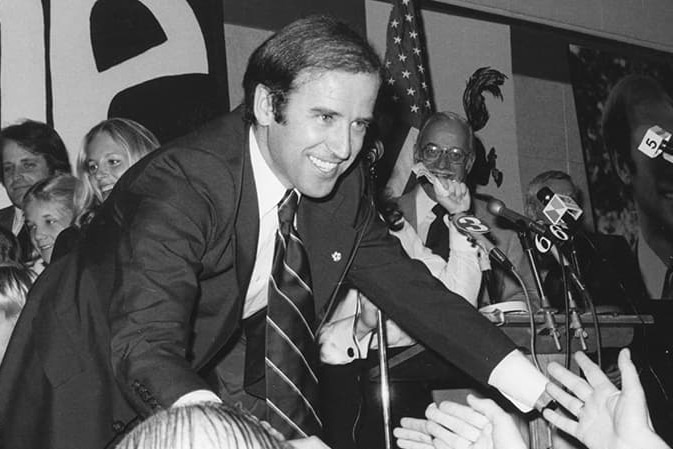 A black and white photo of Joe Biden reaching into an audience