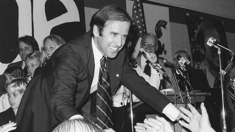 A black and white photo of Joe Biden reaching into an audience
