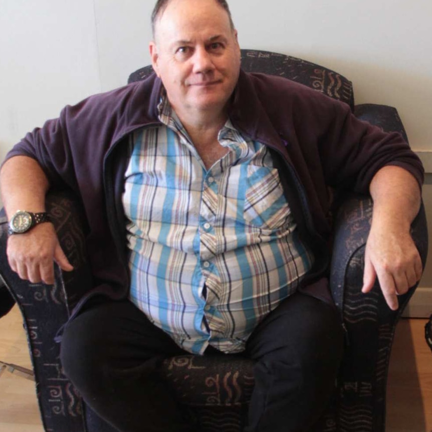 A man sitting on a couch looks up at a camera.