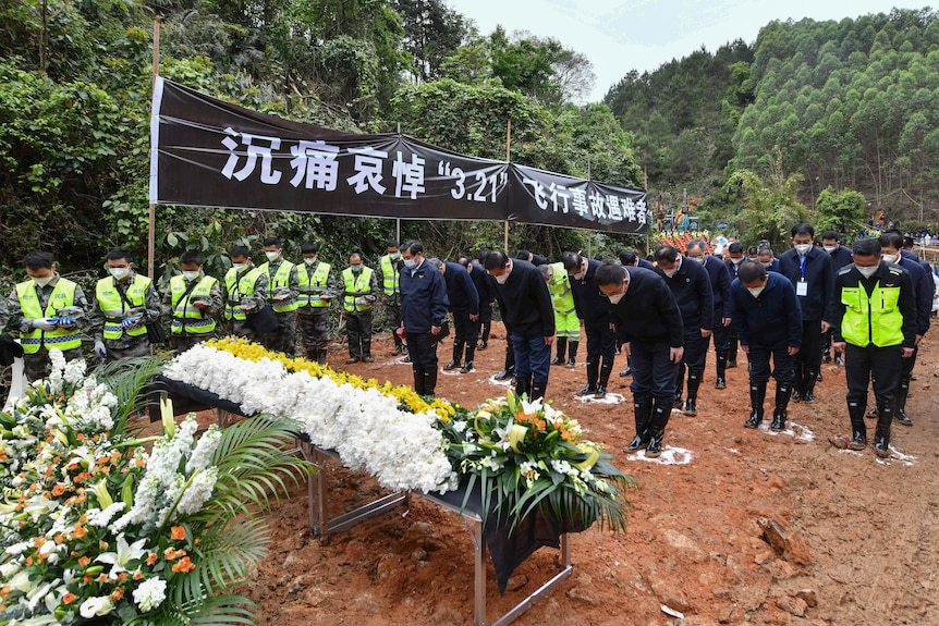 People bow in front of floral arrangement for victims of a plane crash.