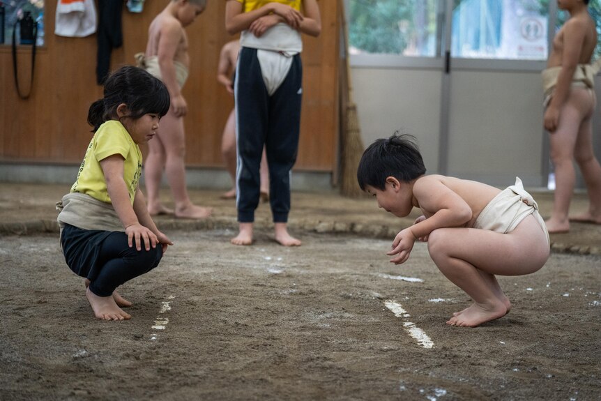 Two children squat in a sumo ring 