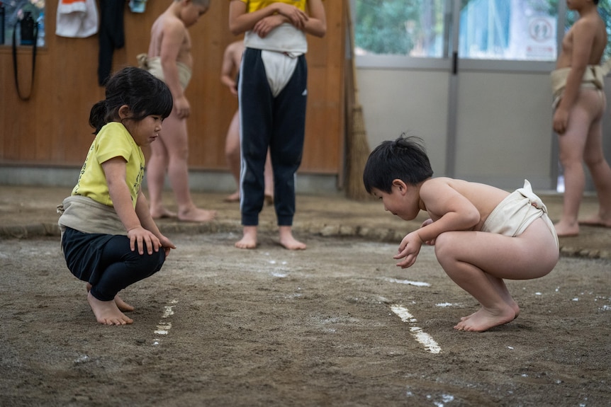 Two children squat in a sumo ring 