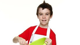 A boy looks at the camera, dressed in a chef's apron