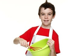 A boy looks at the camera, dressed in a chef's apron