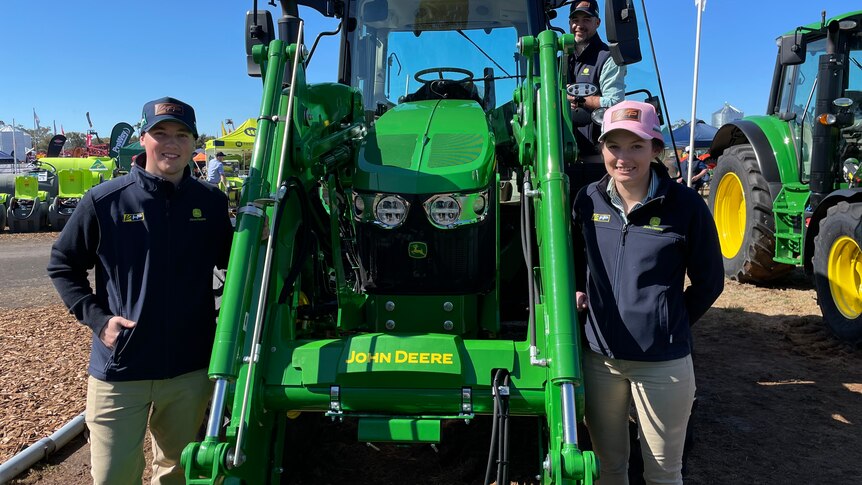 Two men and a woman surround a green tractor.