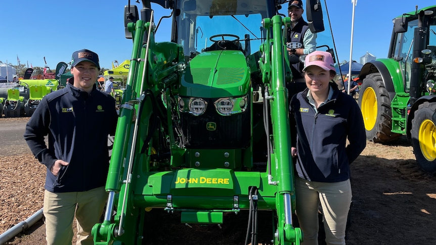 Two men and a woman surround a green tractor.