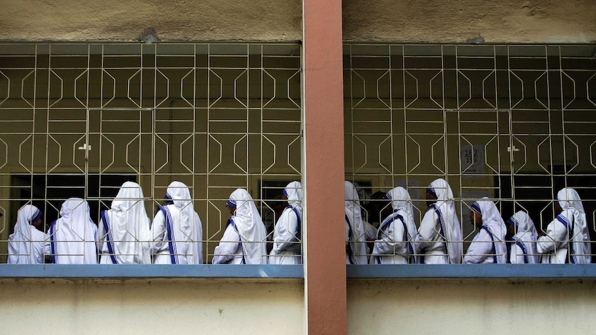 Group of nuns stand on a balcony, all facing away