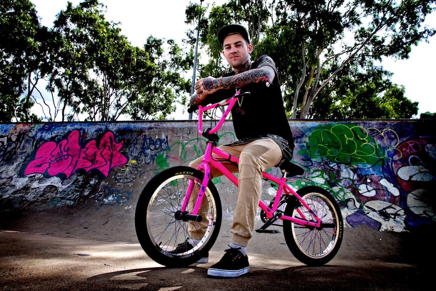 A man sits on a bright pink BMX in the middle of skate park