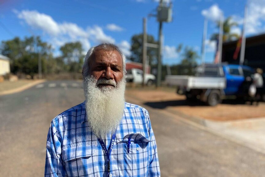 A man wearing a checked shirt with a long white beard stands on a street