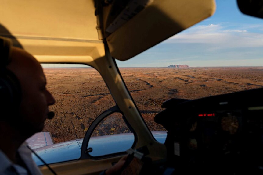 A pilot is seen in the cockpit with Uluru in the backdrop.