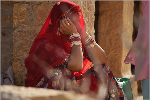 An Indian woman covered in a red veil sits with her head in her hands.