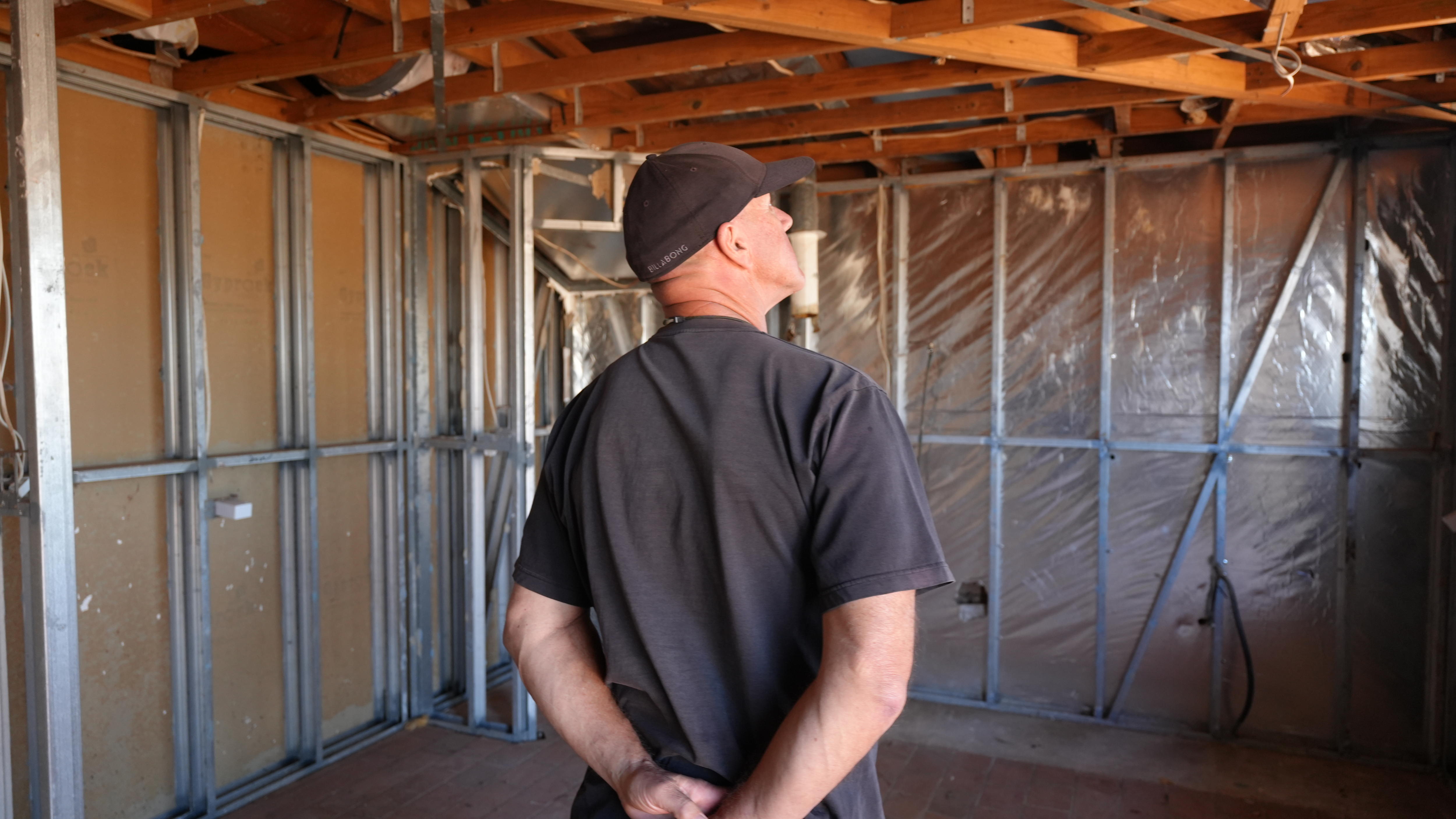 A man in a black cap staring at the damages in the interior of his house.