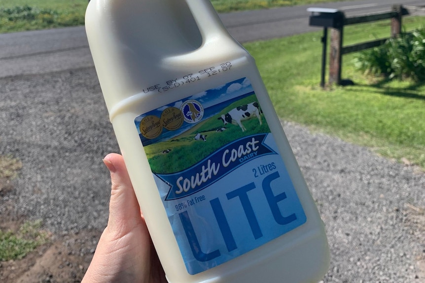 a two-litre milk bottle being held in a person's hand with a farm in the background
