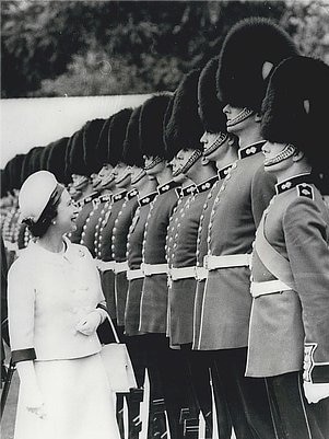 A black and white photo of Robert Krouse dressed in his royal guard uniform as the Queen walks by