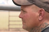 a close-up photo of a man looking away from the camera, he's wearing a cap and has a silver ear stud and neck tattoos