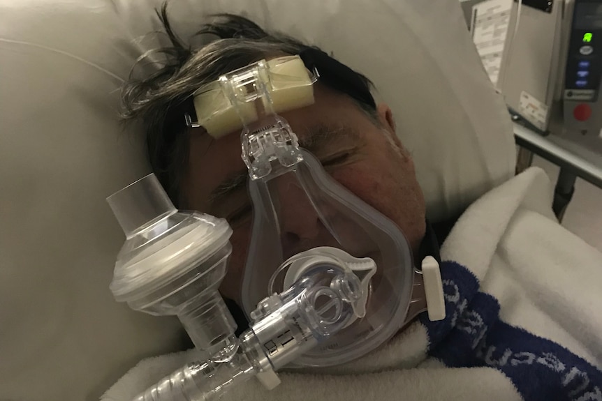 A man in a hospital bed wearing breathing apparatus.