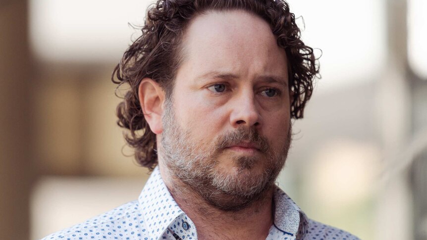 A headshot of a man in a white spotted shirt.