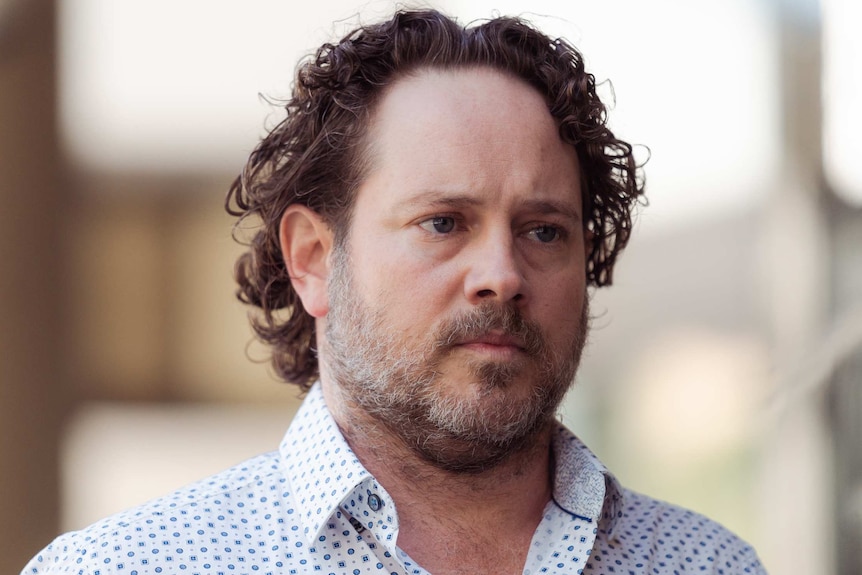 A headshot of a man in a white spotted shirt.