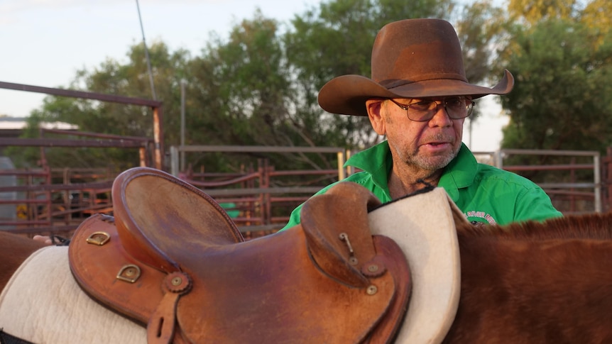 Man wearing a hat and green shirt standing next to a horse.