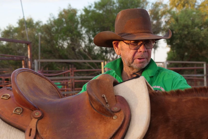 Man wearing a hat and green shirt standing next to a horse.