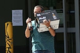 A man carries a carton of beer and a bottle of spirits out of a bottle shop in Perth.