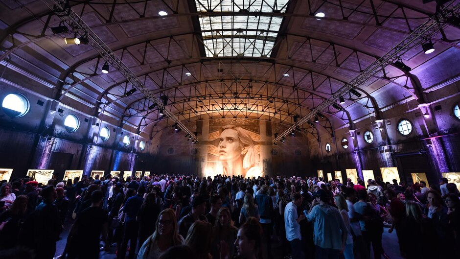 A painting of a woman covers a wall in an old movie theatre filled with people attending Rone's exhibition opening