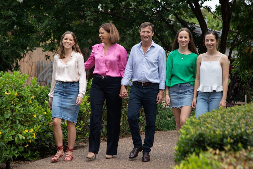 Deb and Jason holding hands, walking through a garden smiling with their three daughters