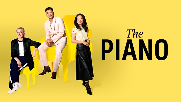 A man and two women standing next to a  piano on a yellow graphics background