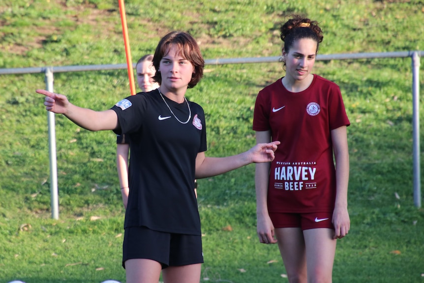 A woman in dark clothing gives some soccer advice to a younger player.