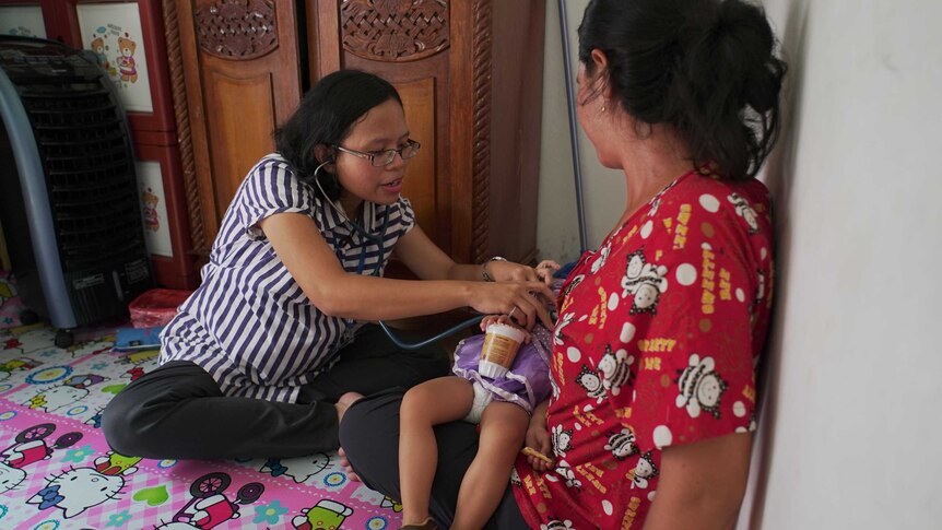 Ana Oktariana holds a stethoscope to the chest of a small two-year-old girl.