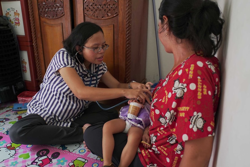 Ana Oktariana holds a stethoscope to the chest of a small two-year-old girl.