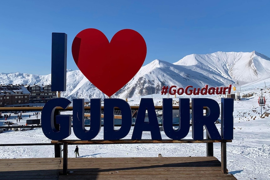 A sign that says 'I Love Gudauri' sits in front of mountains with snow on them.