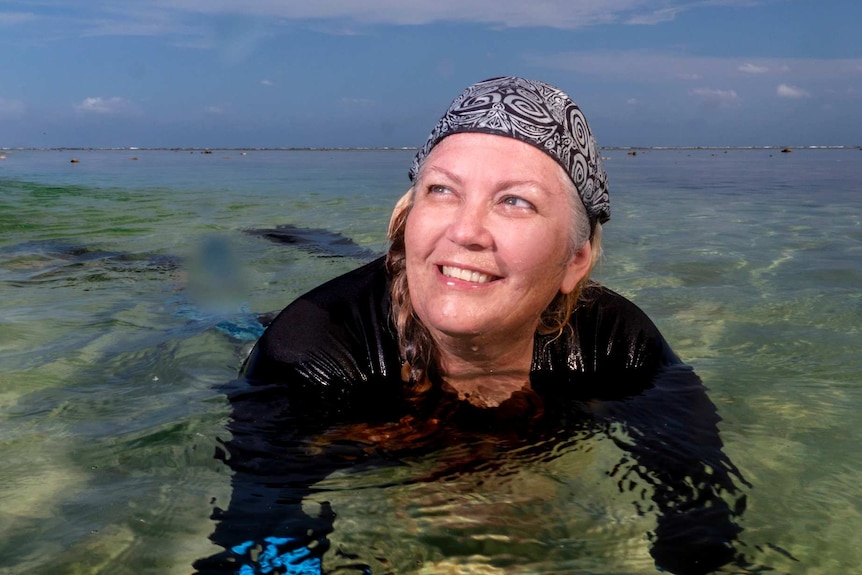 A woman lays in shallow water in diving gear.