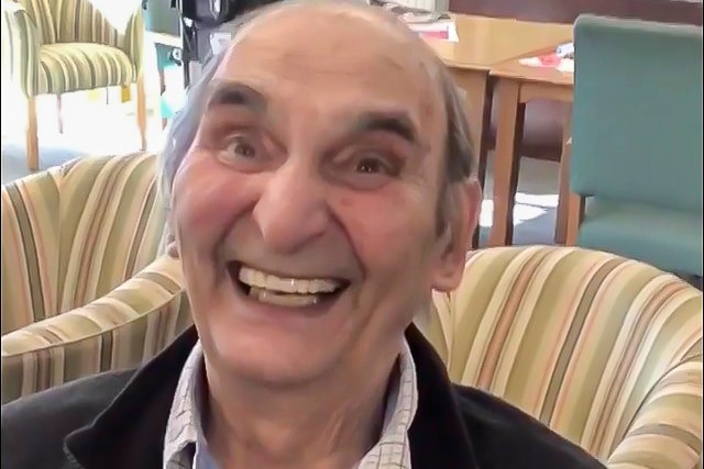 An elderly man smiling comically at the camera