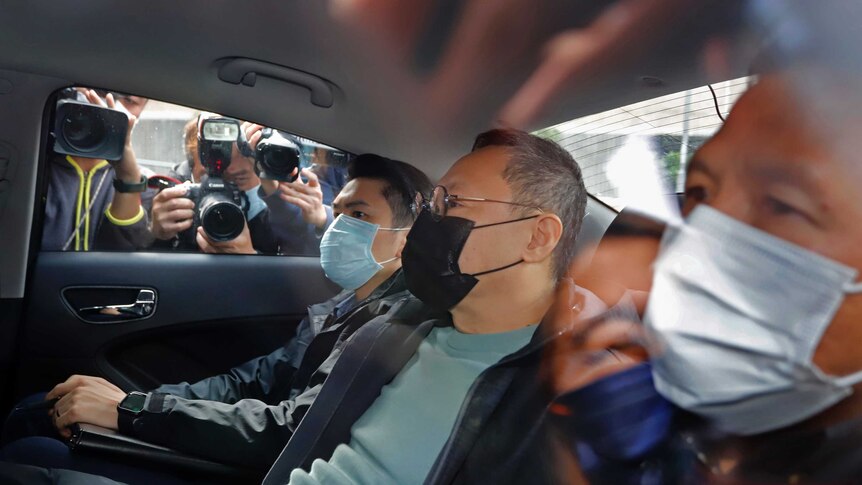 Benny Tai sits in a car after being arrested by police in Hong Kong. Reporters are taking photos through the windows.