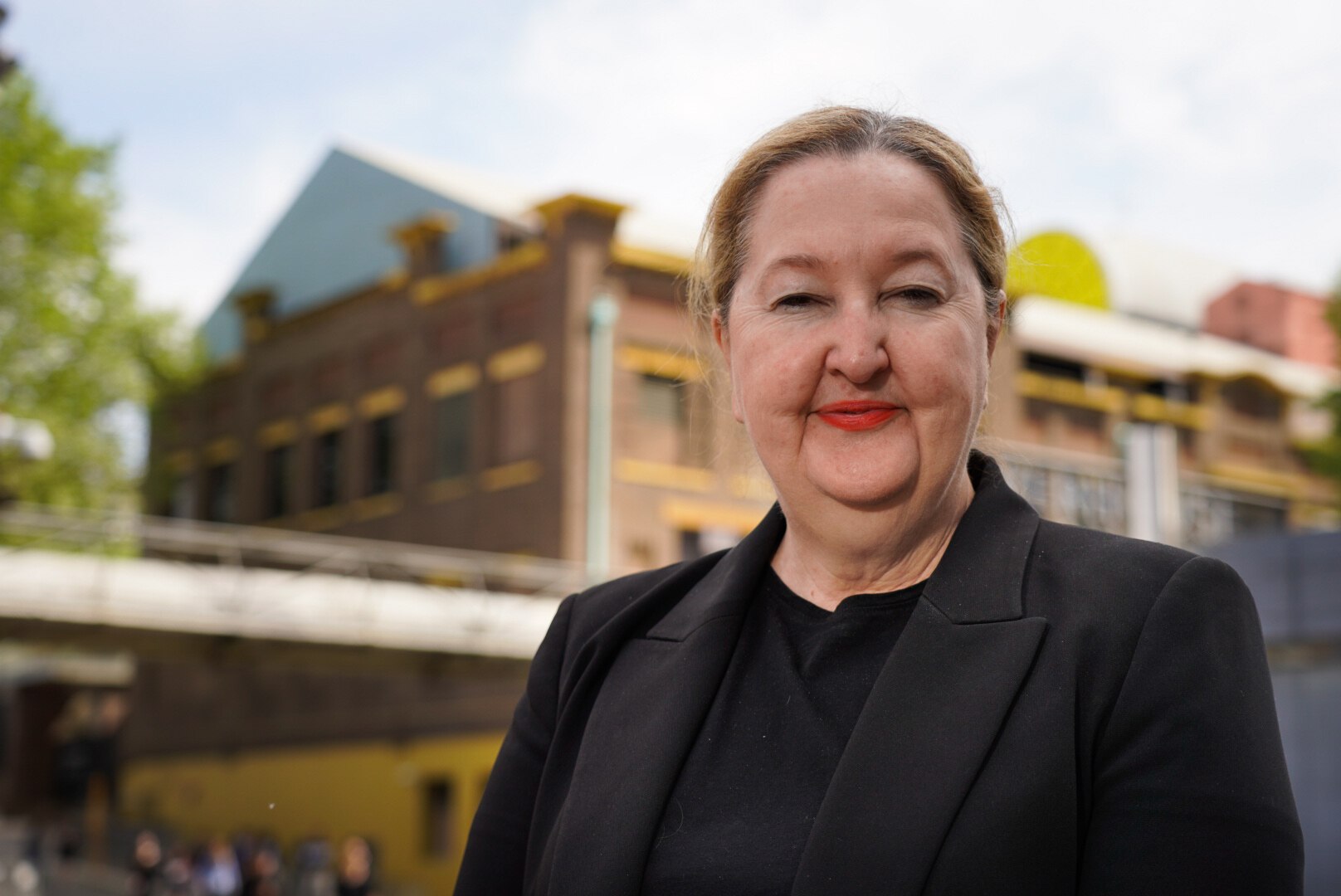 A middle-aged woman wearing black smiles at the camera while standing outside a building.
